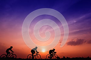 Silhouette three men ride bikes at sunset with orange-blue sky background photo