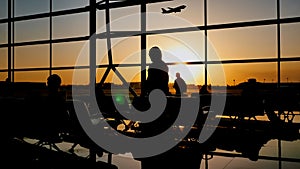 Silhouette of a tourist guy watching the take-off of the plane standing at the airport window at sunset in the evening