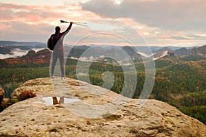 Silhouette of tourist with poles in hand. Sunny spring daybreak in rocky mountains. Hiker with sporty backpack stand on rock