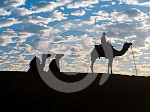 Silhouette of tourists enjoying camel desert safari with beautiful sky