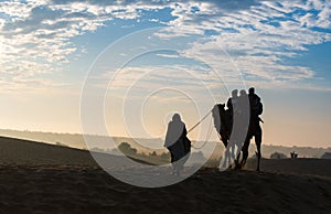 Silhouette of tourists enjoying camel desert safari with beautiful sky