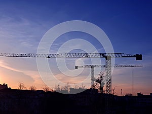 The silhouette of a tower crane against the background of the sky and the city.