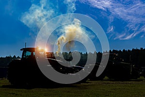 Silhouette of a tractor in the field with the included glowing headlights at night on a background of the sky