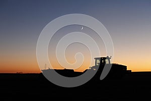 A silhouette of a tractor harvesting potatoes at night