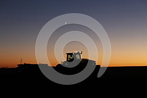 A silhouette of a tractor harvesting potatoes at night