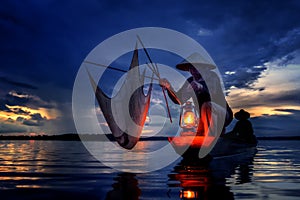 Silhouette of traditional fishermen throwing net fishing lake in the mystic clound at sunset