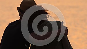 Silhouette traveler couple admiring the sea view. Rear view of man and woman hugging each other at sunset or sunrise on a deserted