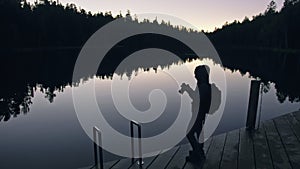 Silhouette traveler photographing scenic view in forest, river. Wood pier. One woman shooting nice dark magic night look