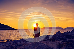 Silhouette of traveler who stands on the rock seashore