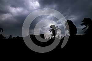 A silhouette of trees and houses with sky full of dark clouds above. Calmness before the storm