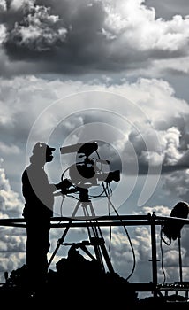 Silhouette of a TV cameraman against cloudy sky