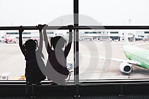 Silhouette of two asian child girls with backpack looking at plane and waiting for boarding in the airport