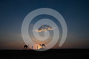 Silhouette of two cameleers and their camels at sand dunes of Thar desert