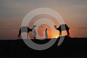 Silhouette of two cameleers and their camels at sand dunes of Thar desert