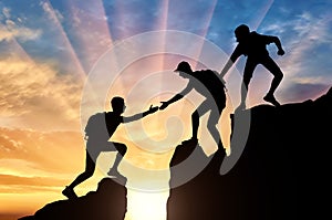 Silhouette of two climbers in the mountains help another climber to overcome the obstacle