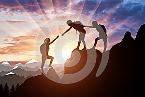 Silhouette of two female mountaineers helping another female mountaineer to overcome the obstacle in the mountains