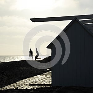 Silhouette of two friends guys playing on a sunset background on a beach in evening.  The boys silhouettes on the beach at sunset