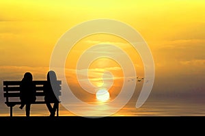 Silhouette of two friends sitting on wood bench near beach