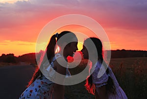 Silhouette of two little girls smiling on sunset. Sisters enjoyed a Holiday over blurred summer nature. Hhappy childhood concept