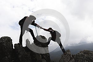 Silhouette of Two male hikers climbing up mountain cliff and one of them giving helping hand. People helping and, team work