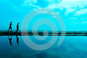 Silhouette of two man running at the beach