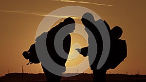 The silhouette of two man standing on the top of mountain with backpacks and use phone for navigation. Lifestyle, travel