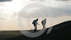 The silhouette of two man on the top of mountain with backpacks and other gear expressing energy and happiness. Two