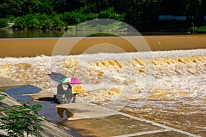 Silhouette of two men sitting under colorful umbrellas fishing in the turbulent muddy water