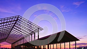 Silhouette two metal industrial building outlines in construction site area against sunset sky background