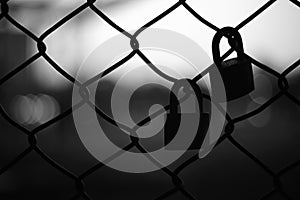 Silhouette of two pad locks on chain link fence