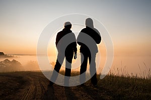 Silhouette of two peple looking at sunrise on foggy valley