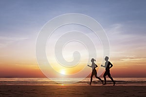 Silhouette of two runners running on the beach at sunset