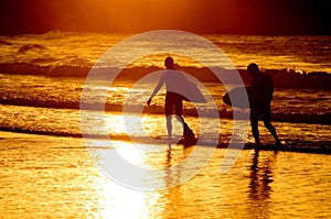 Silhouette of two surfer at yellow sunset