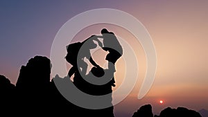 Silhouette of two tourists lends helping hand climb cliffs mountains helping hand. teamwork helping hand business travel