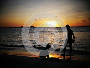 Silhouette of two unrecognizable boys playing in the beach at sunset