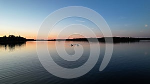 Silhouette of two women on a SUP board in the evening twilight on a calm lake.