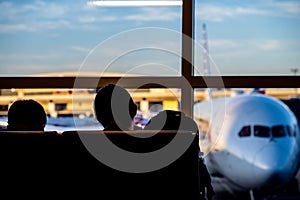 Silhouette of two young adults slouched in an airport terminal with a defocused airplane out the window