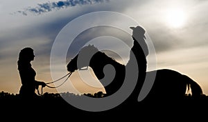 Silhouette of two young girls with a hat and a horse on the background of the sunset sky