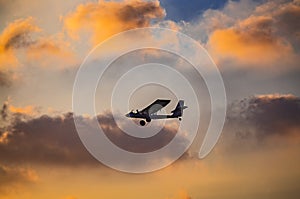 Silhouette of ultralight microlite aircraft flying with a pilot and a passenger against sunset sky