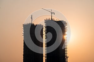 Silhouette of under construction building against sunset with crane on roof showing rapid real estate infrastructure growth in