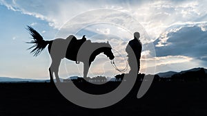 Silhouette of an unidentified man standing with a horse in dusk