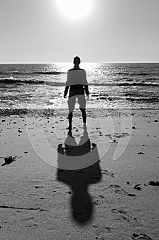 Silhouette of unknown man standing on beach black and white. Loneliness and solitude concept. Men silhouette on sea background.