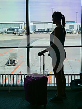 SILHOUETTE: Unknown young woman standing by the window and looking at airport