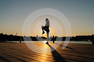 Silhouette of unrecognizable fitness woman exercising and stretching legs before running or working out on beautiful