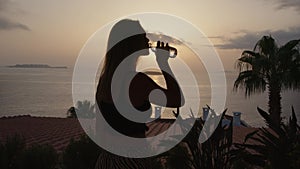 silhouette of unrecognizable girl drink water from transparent bottle at sunset, in background ocean or sea with island