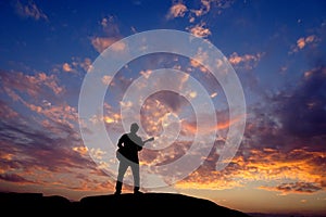 A silhouette unrecognizable guitarist playing guitar on top of a rock during sunset