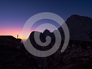 SILHOUETTE: Unrecognizable hiker faces the rocky mountain at golden sunrise.