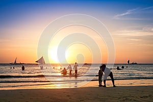 Silhouette of unrecognizable tourists and local people with father and son taking selfie at Boracay beach during sunset -