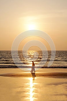 Silhouette of an unrecognizable woman in traditional Indian clothing walking on a golden sandy beach at sunset