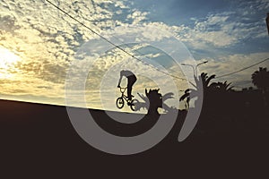 Silhouette unrecognizable Young man doing ramp jump stunt on bmx bicycle on sunset.